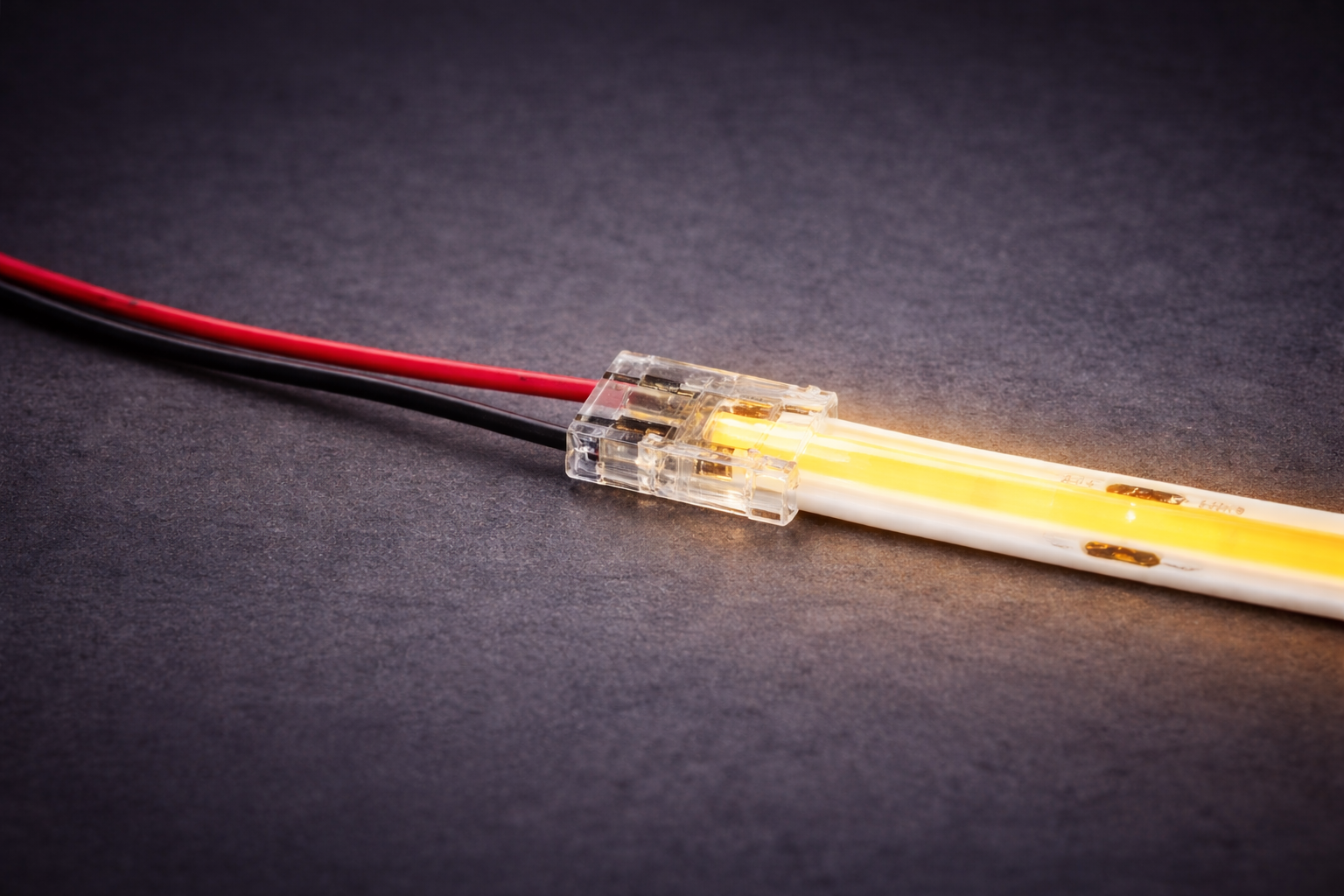 Transparent wire-to-strip connector attached to an illuminated COB LED strip, with red and black power wires extending from one side, shown on a dark background.